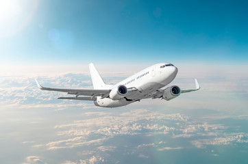 Naklejka na ściany i meble Passenger white airplane flies in a blue sky with a bright sun.