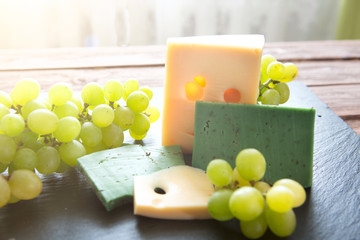 Various types of cheese with green grapes on black slate cheeseboard on table