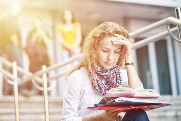 Young smiling student woman writing and reading book on stairs of university or college, preparing for exams. Education concept, copy space