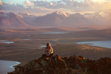 Girl sits on big rock against mountains and lakes