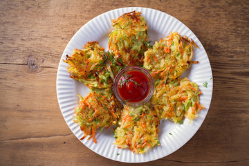 Potato Zucchini and Carrot Cakes. Vegetable fritters, latkes, draniki. Vegetable pancakes on white plate on wooden table. overhead, horizontal