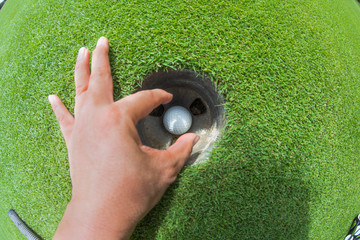 view of fish eye lens on the golf ball in the hole going to takes-out bt hand of golf player after...