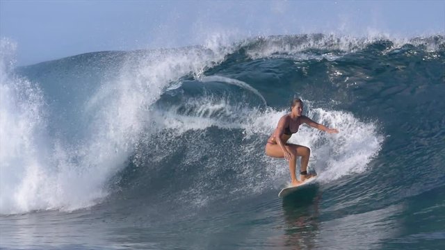 SLOW MOTION: Surfer girl in bikini riding big barrel overhead waves on a perfect sunny day. Extreme sportswoman riding her surfboard along a large barrel wave dives into the deep blue ocean water.