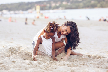 Young mixed race family sitting and relaxing at the beach on beautiful summer day.Mother playing...