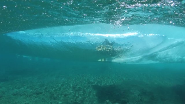 SLOW MOTION, UNDERWATER: Unrecognizable pro surfer on epic vacation riding a big barrel wave on sunny day in Fiji. Unknown experienced surfboarder carving a spectacular turquoise colored ocean wave