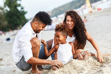 Young mixed race family sitting and relaxing at the beach on beautiful summer day.Playing in the...