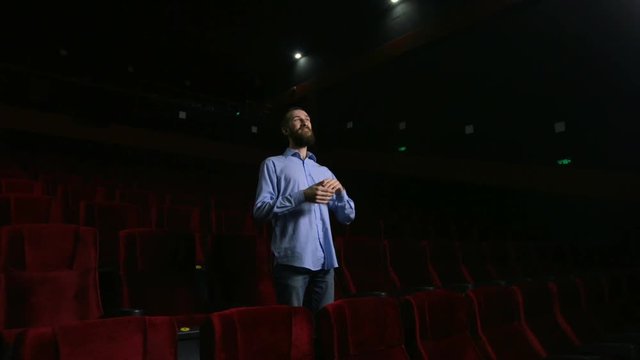 Single man sitting in comfortable red chairs in dark cinema theater and applauds.