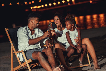 Young mixed race family sitting and relaxing at the beach on beautiful summer night.They sitting on...