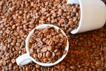 Two coffee cups filled with coffee beans. One cup lies on its side
