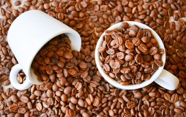 Two coffee cups filled with coffee beans. One cup lies on its side