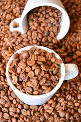 Two coffee cups filled with coffee beans. One cup lies on its side