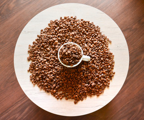 A coffee cup with coffee beans is on a light round table