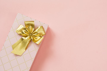 Female gift box with golden ribbon on punchy pastel pink. Birthday. Copy space.