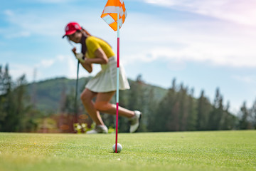 golf ball running through the hole on green most successfully after putted by player, woman golf player is in exciting and cheerfully forward in background