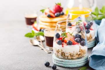 Oatmeal granola with berries and yogurt and panccakes on light gray concrete background. Healthy breakfast food concept with copy space.