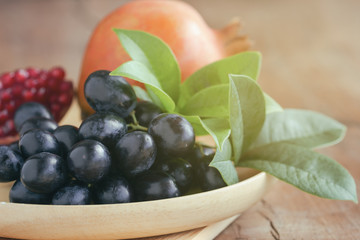Fresh pomegranate and seedless red grape and on wooden plate put on wood table in side view with copy space for background or wallpaper. Delicious and healthy fruit with sweet taste and juicy.