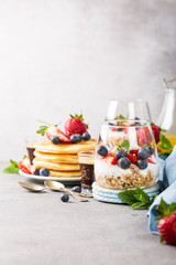 Healthy breakfast with oatmeal granola with berries and yogurt and panccakes on light gray concrete background. Healthy food concept with copy space.