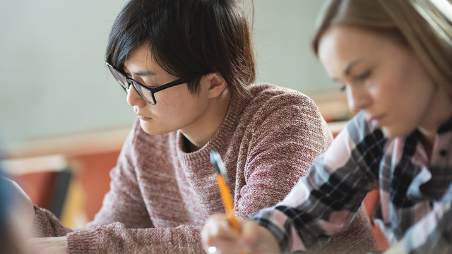 Shot of a Row of Multi Ethnic Students in the Classroom Taking Exam/ Test/ Writing in Notebooks. Bright Young People Study at University.