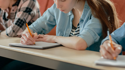 Moving Footage of a Row of Multi Ethnic Students in the Classroom Taking Exam/ Test. Focus on Holding Pens and Writing in Notebooks. Bright Young People Study at University.