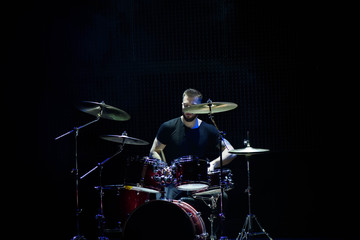 Plakat Drummer in a cap and headphones plays drums at a concert under white light in a smoke