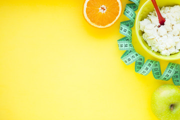 Fruits, curd, measuring tape, water and muesli on the yellow background. Weight loss, diet controlled healthy food concept background. Top view, close up.