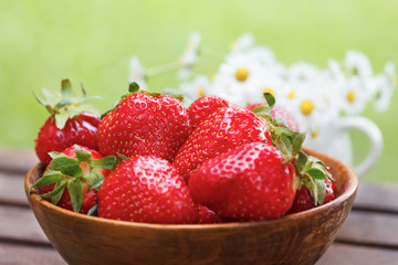 Fresh strawberries in a bowl on wooden table with natural green background