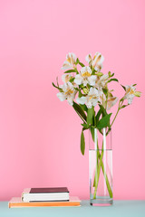 two books and bouquet of alstroemeria flowers on table on pink
