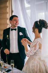 Newlywed Couple Cheerful Wedding Reception. Bride and groom kiss near wedding table. Listening congratulations.
