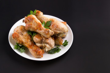 plate of roasted chicken drumstick on a black, dark background