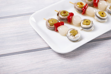 Banderillas of olives with spring onion and anchovies in a white plate on wooden table. Typical spanish food.