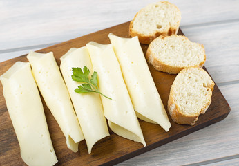 Slices of cheese with round shape next to bread on wooden board. Isolated.