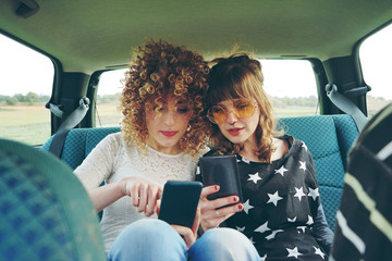 Dos amigas usando sus teléfonos móviles mientras hacen un viaje en coche 
