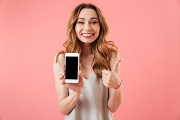 Happy brunette woman in pajamas showing blank smartphone screen