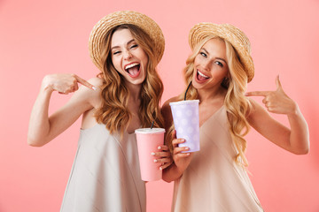 Two laughing pretty women in dresses and hats posing together