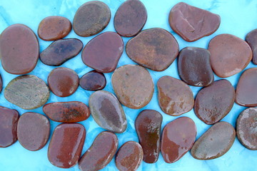 Wet pebbles stones on blue background. Pebbles on blue surface, top view.