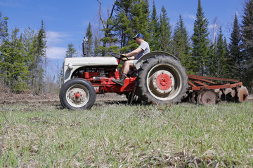 Obraz premium Side view of a man driving a tractor in a field.