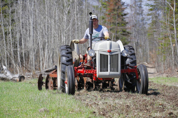 Obraz premium A man driving a tractor to disk a field.