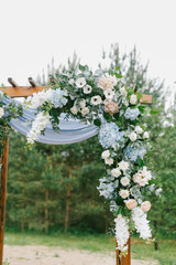Floral arch with blue cloth and wooden elements at a rustic  wedding ceremony