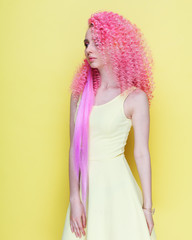 Portrait. Beautiful curly-haired girl posing in studio on a yellow background. Incredible hairstyle with pink curls.