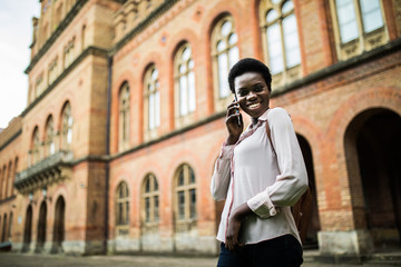 Fototapeta premium Portrait of pretty black woman in urban background talking on phone. Young student talking on phone at campus