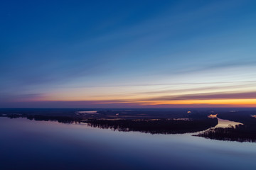 Beautiful river with big island with trees under predawn sky. Bright yellow stripe in picturesque cloudy sky. Early blue sky reflected in water. Colorful morning atmospheric image of majestic nature.