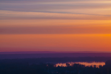 River under varicolored striped warm sky. Horizontal lines of picturesque clouds. Atmospheric background image of lake with reflection of dawn sky.