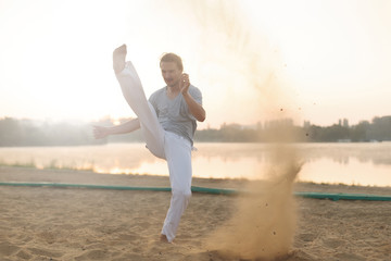 Athletic capoeira performer workout training on the beach sunris