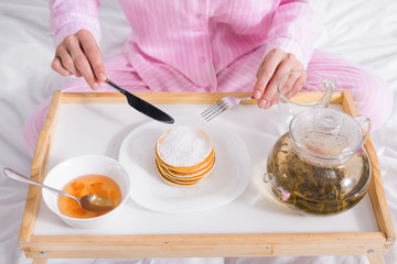 partial view of woman in pajamas having pancakes with jam for breakfast in bed at home