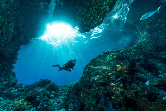 woman diver underwater at the entrance of a cave with sunrays