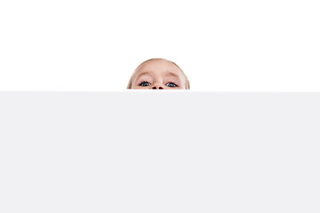 Child face on a white background peeps out from behind a gray fence