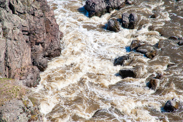 a rough river with rapids in the forest, with splashes of water, under a blue sky, surrounded by forest