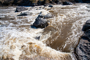 Naklejka premium a rough river with rapids in the forest, with splashes of water, under a blue sky, surrounded by forest