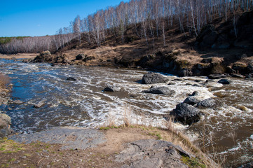 a rough river with rapids in the forest, with splashes of water, under a blue sky, surrounded by forest