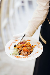 Salads and meat dishes in the hand of the waiter. Serving in a restaurant
